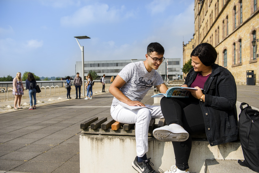 Zwei Studierende lesen draußen gemeinsam ein Buch 