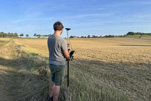 Ein Mann steht mit einem Messgerät am Feldrand.