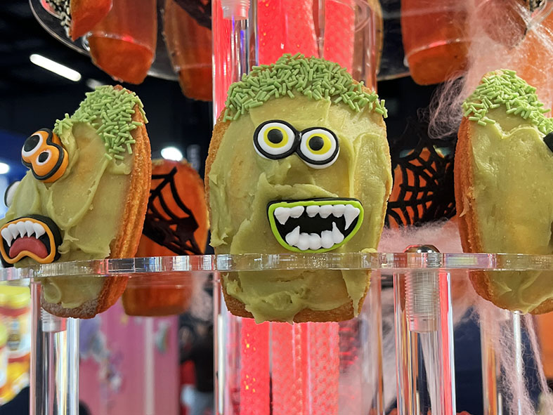 Das Bild zeigt eine Auswahl an buntem Gebäck, das mit kreativen Halloween-Motiven verziert ist. Geister und Spinnennetze aus Zuckerguss schmücken die Kekse, die auf einem dekorativ arrangierten Messestand präsentiert werden. Das Bild bietet einen kleinen Einblick in das, was die Studierenden der Ökotrophologie bei ihrem Besuch auf der anuga-Messe (bedeutende Messe der Ernährungs- und Lebensmittelwirtschaft) in Köln erleben konnten. 