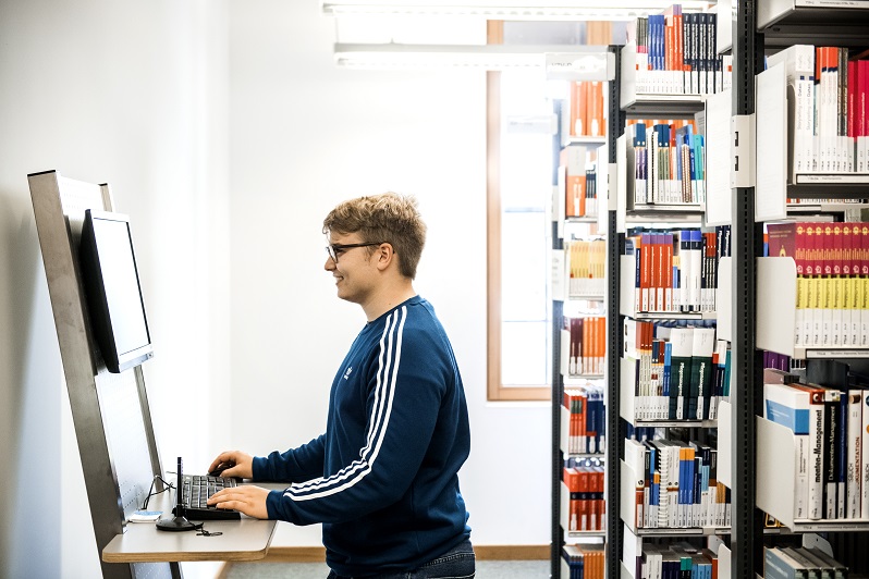 Ein Student nutzt einen festinstallierten Computer in der Bibliothek am Campus Lingen, um herauszufinden, wo das von ihm gesuchte Buch steht.