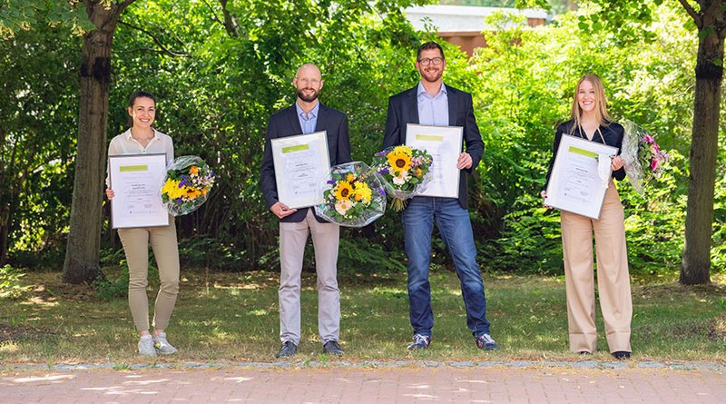 Vor grünen Bäumen stehen die Preisträgerinnen und Preisträger mit der Urkunde und einem Strauß Blumen. Von links nach rechts: Veronika Markus (B.Sc.), Fabian Moll (M.Sc.), Holger Nienaber (M.Sc.), Nora Cryns (B.Sc.)