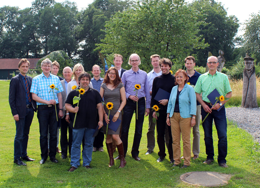 Auf dem Bild sieht man 15 Personen, teilweise mit Sonnenblumen und blauen Mappen in der Hand.