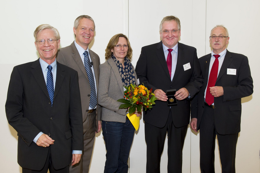 Auf dem Bild sieht man eine Gruppe von fünf Personen. Der Mann in der mitte hält eine Medialle in der Hand.