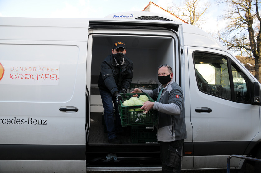 Ein Mann übergibt einem zweiten Mann vor einem Transporter Gemüse