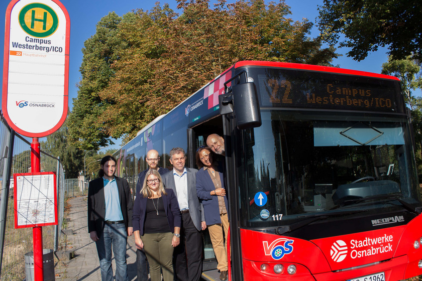 Das Bild zeigt fünf Personen an einer Bushaltestelle, die halb in einem Bus stehen.