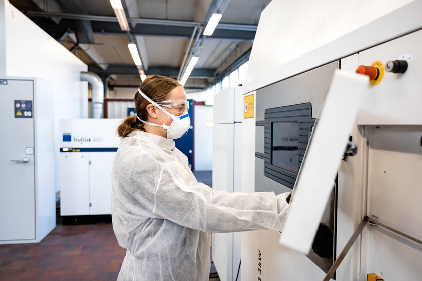 Frau in Schutzkleidung vor einem 3D-Drucker für Metalle. 