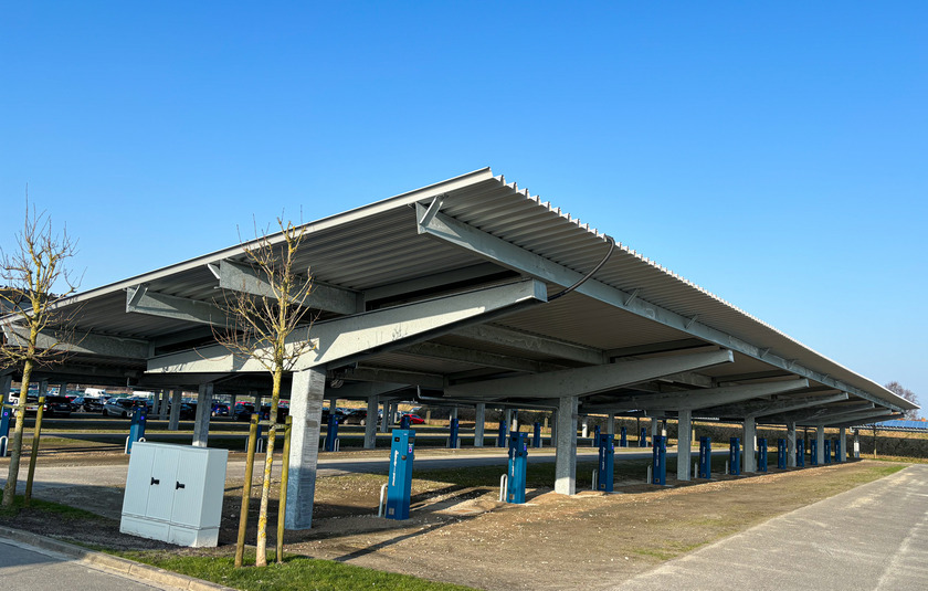 Überdachter Parkplatz mit E-Ladesäulen. Auf den Dächern ist eine PV-Anlage angebracht.