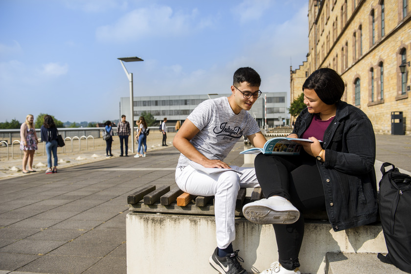Zwei Studierende lesen draußen gemeinsam ein Buch