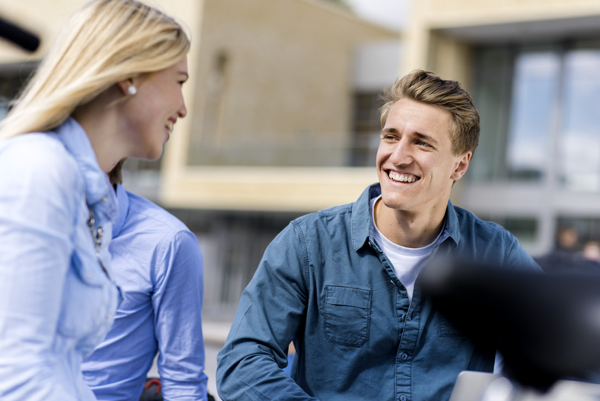 Studentin und Student sitzen vor der Mensa und führen ein Gespräch.