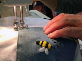 Mit der Nähmaschine wird das Motiv einer Biene auf ein weißes T-Shirt genäht.