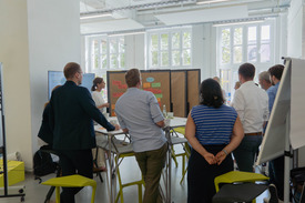 Arbeitsgruppe aus Männern und Frauen im Workshop stehen vor einem Whiteboard.