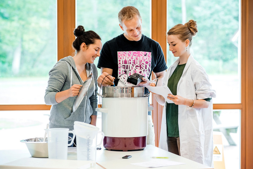 Studierende stehen im WABE Zentrum um einen Topf und prüfen die Temperatur des Inhaltes