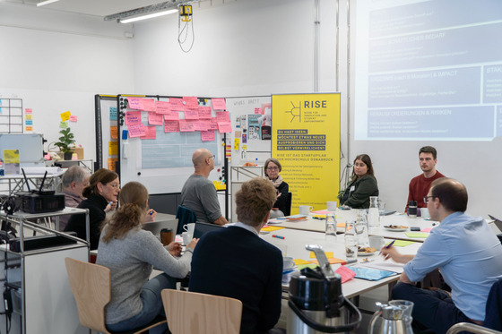 Eine Gruppe von Männern und Frauen sitzen vor einem Whiteboard mit zahlreichen Post-its voller Ideen.