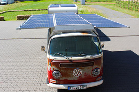 Alter roter Volkswagen-Bus mit großen Solarpanelen auf dem Dach, geparkt auf gepflastertem Platz