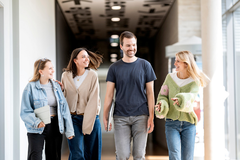 Auf dem Foto gehen vier Studierende zusammen durch einen Flur und lachen dabei.