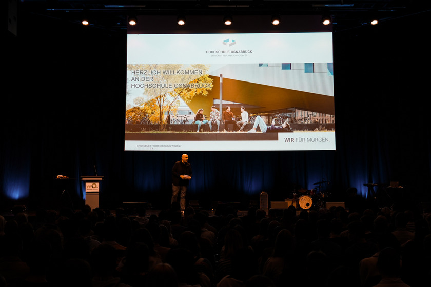 Moderator Benjamin Häring steht in der OsnabrückHalle auf der Bühne vor den Erstsemestern.