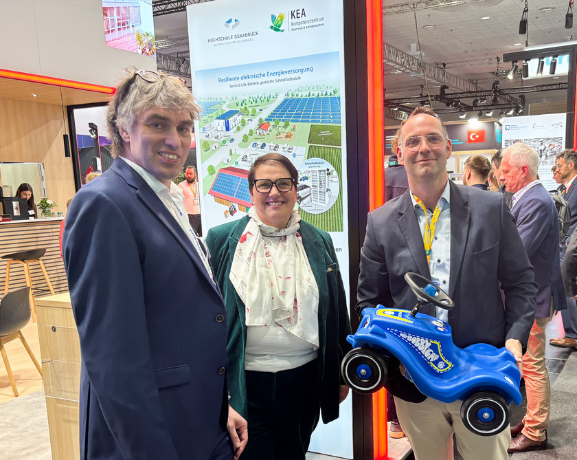 Drei menschen lächeln in die Kamera. Einer hält ein blaues Rutschauto. 