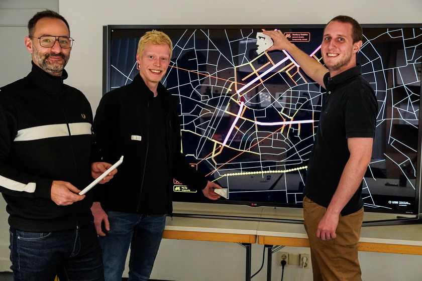 Drei der Teammitglieder vor einem Moniter, der die digitale Komponente des Projektes zeigt. 