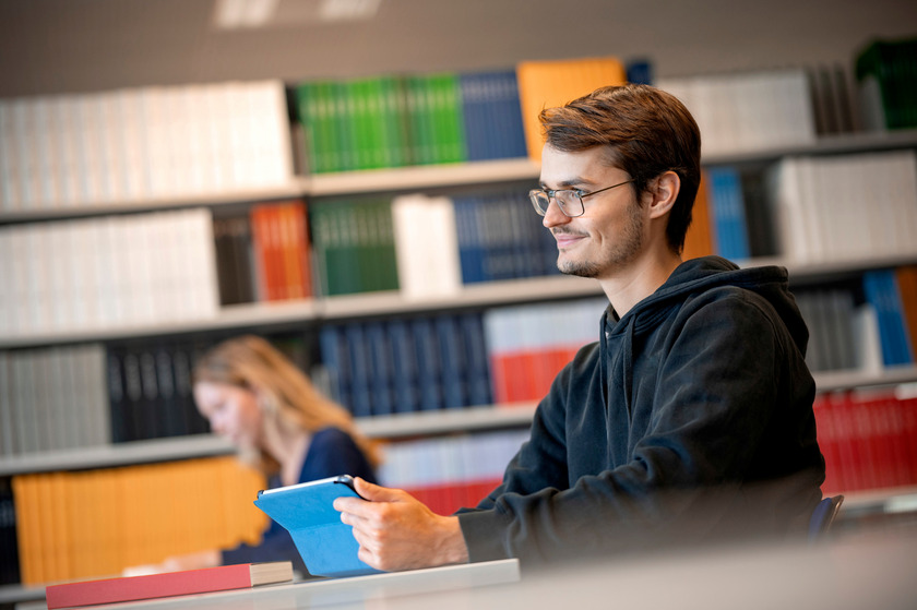 Student in der Bibliothek mit Tablet in der Hand