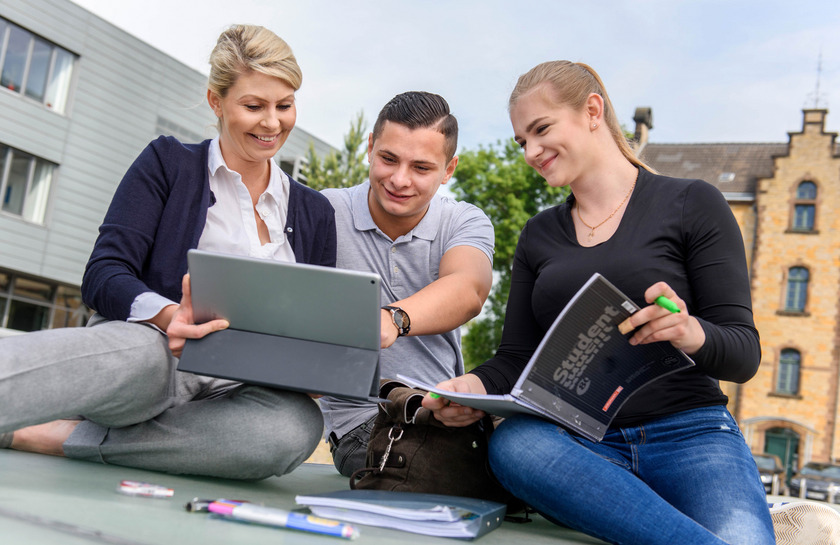 Drei Studierende sitzen mit Lehrbüchern und Tablet auf dem Caprivi-Campus