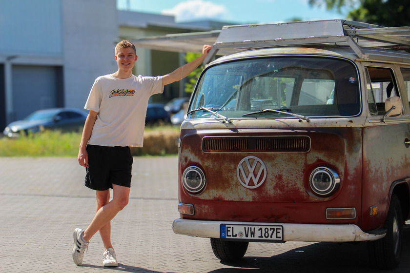 Ein jungermann lehnt an einen roten VW-Bulli