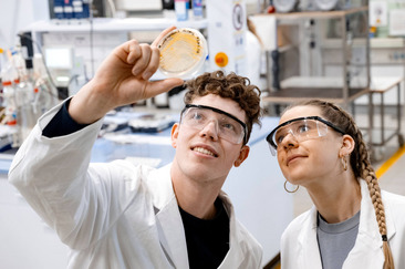 Zwei Studierende schauen sich eine Petrischale in einem Labor an.