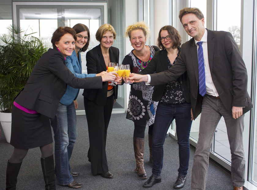 Gruppenbild Man sieht eine Gruppe von Menschen, die anstoßen.