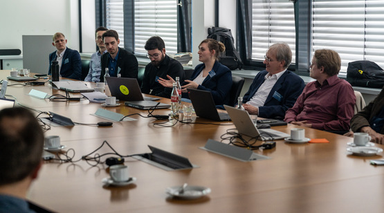 Gruppe von menschen sitzt um einen großen tisch und unterhält sich.