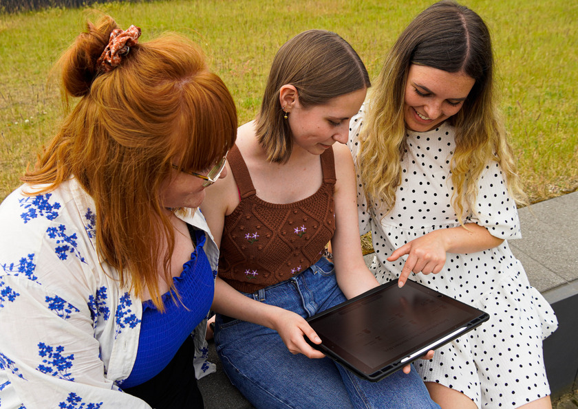 Die drei Studentinnen Lea Evers, Vanessa Buschhorn und Isabell Kostrowski schauen gemeinsam auf ein Tablet, auf dem ihre selbst entwickelte App geöffnet ist.