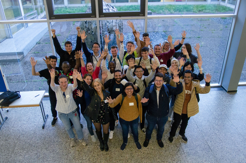 Eine Gruppe von Menschen unterschiedlicher Geschlechter schaut lachend in die Kamera. Manche haben die Arme in der Luft.
