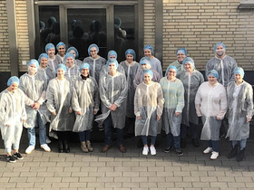 Eine Gruppe von Studierenden steht in voller Schutzkleidung vor dem Eingang zum Verwaltungsgebäude der Firma AVO in Belm.