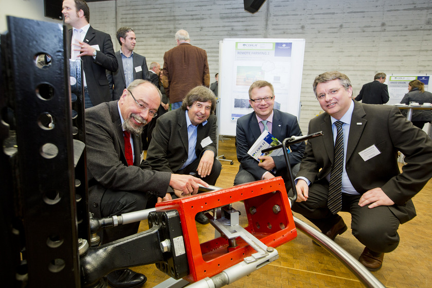 COALA Auf dem Bild sieht man vier Männer, die vor einem roten Roboter knien.