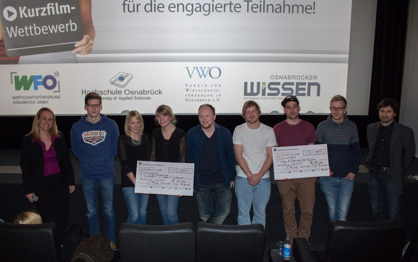 Auf dem Bild sieht man einen neun Personen mit Schecks in der Hand vor einer Kinoleinwand.