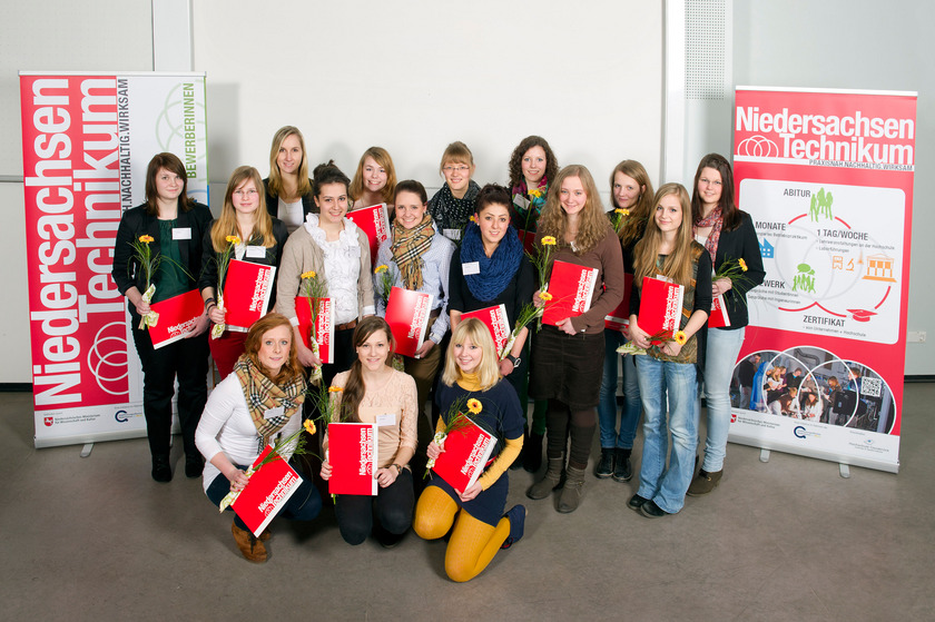 Das Bild zeigt eine Gruppe von 16 jungen Mädchen, die rote Mappen und Blumen in den Händen halten.