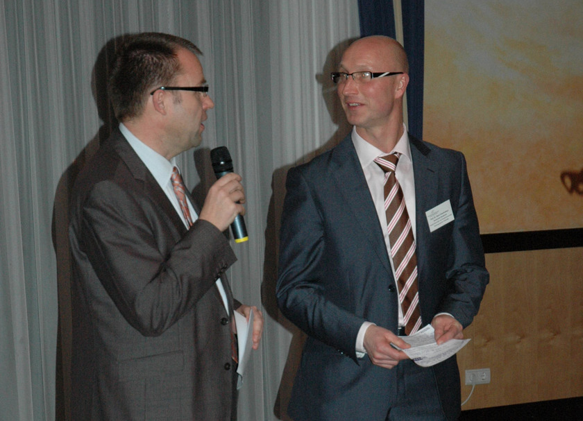 Auf dem Bild sieht man zwei Männer in Anzügen mit Mikros in der Hand.