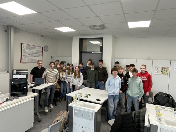 Gruppe von Schülern mit den beiden Hochschulmitarbeitern in einem Chemie-Raum.