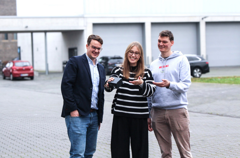 Drei Menschan schauen gemeinsam auf einen Laserscanner.