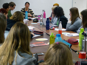 Eine Gruppe Studierender sitzt mit Frau Steins an einem langen Tisch. Sie führen ein Gespräch.