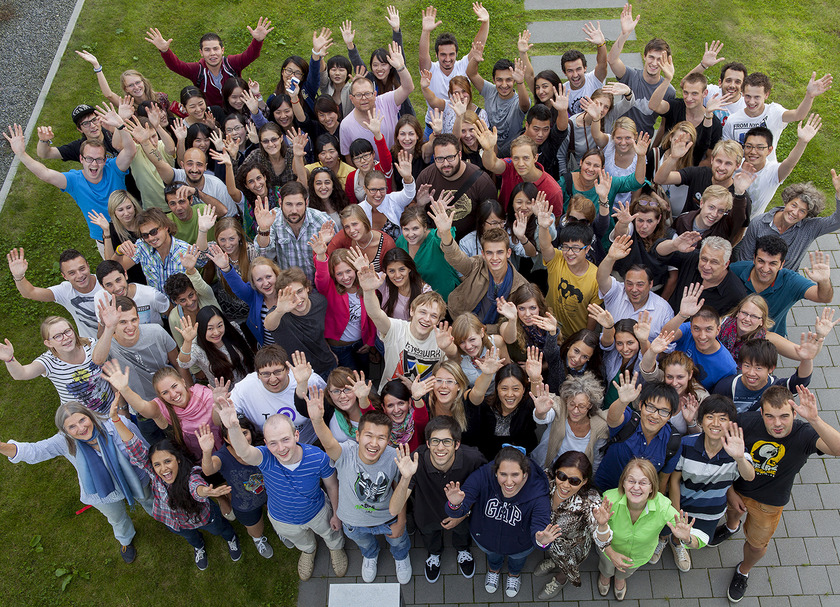 Das Bild zeigt eine große Gruppe junger Menschen, die alle die Arme jubelnd nach oben strecken und lachen.