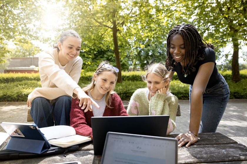 Auf dem Foto sitzen vier Studentinnen draußen an einem Tisch und schauen gemeinsam auf einen Laptop.