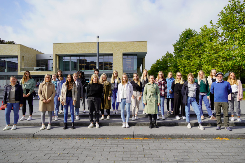 Gruppenbild: 24 Studierende stehen auf dem Mensavorplatz vor der Mensa auf den Stufen.