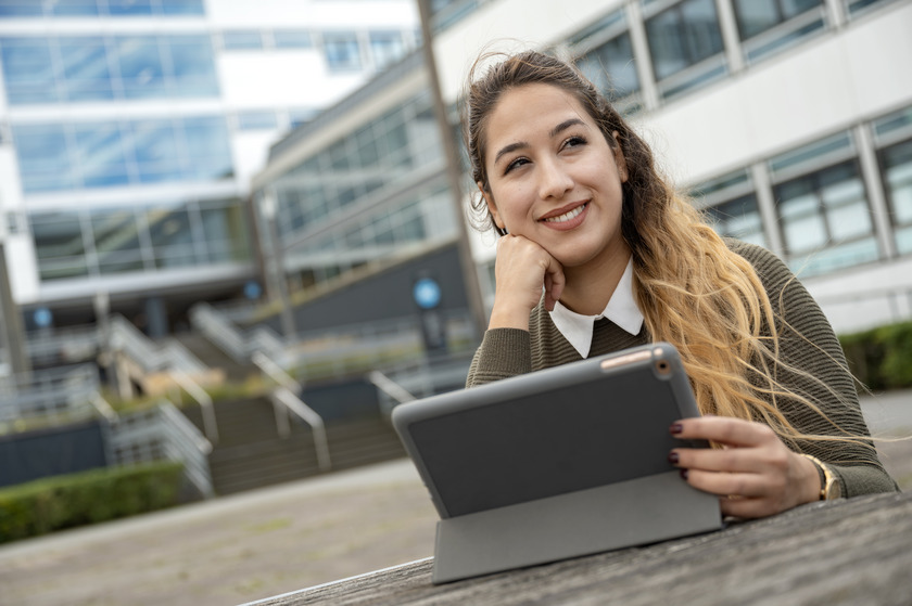 Eine Studentin sitzt draußen an einem Tisch vor ihrem Tablet.