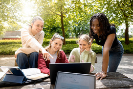 Am Campus Caprivi gibt es viele Möglichkeiten um auch Draußen zu lernen. Vier Studierende sitzen gemeinsam an einer Sitzgruppe und schauen auf einen Laptop.