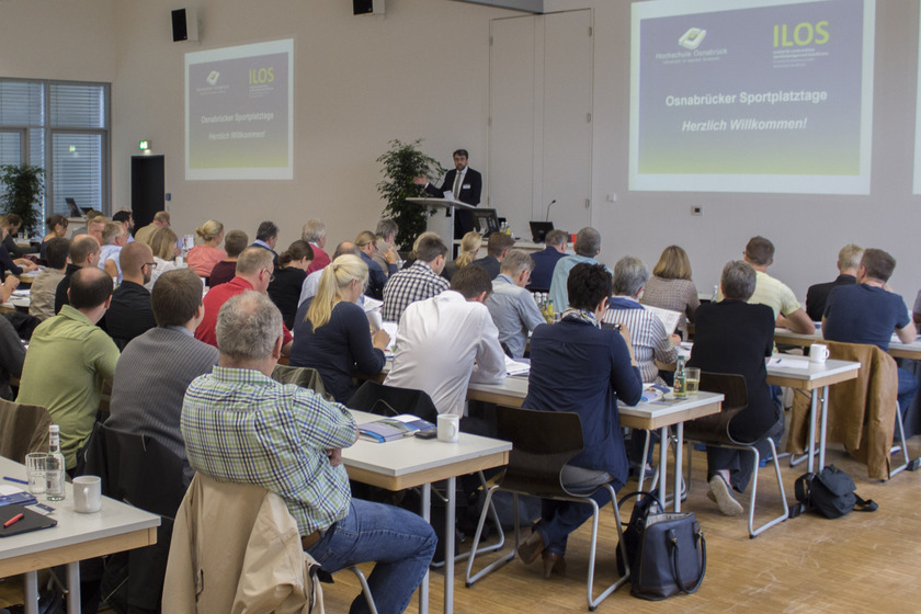 Das Bild zeigt eine Gruppe von Personen an Tischen in einem Seminarraum.