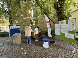 Zwei Frauen stehen vor einer mobilen Küche auf Rädern, rechts und links daneben stehen Stellwände mit Postern und Grafiken zur Information.de 