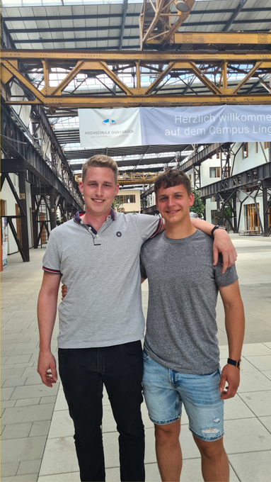 Felix Muke und Lennart Elfert stehen am Campus. Felix hat einen Arm über Lennarts Schultern gelegt. 