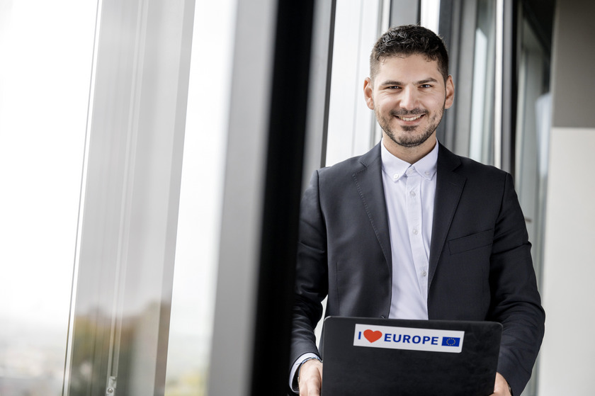 Auf dem Bild ist der ehemalige Master Student Panourgias Papaioannou mit seinem Laptop an einem Fenster und schaut in die Kamera. 