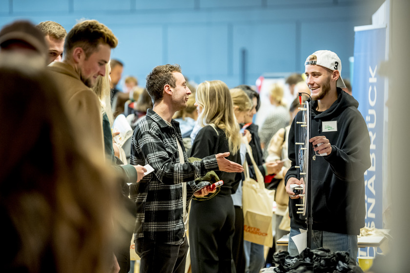 Zwei Studenten unterhalten sich an einem Infostand, an dem ein Glücksrad steht.