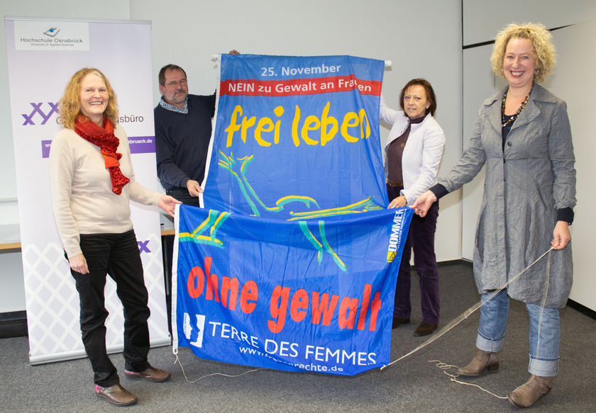 Man sieht vier Personen, die eine große Fahne halten.