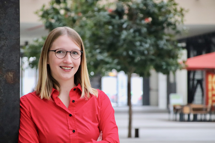 Myriam Erath steht an einen Pfeiler gelehnt in der Halle des Campus Lingen und schaut lächelnd in die Kamera.
